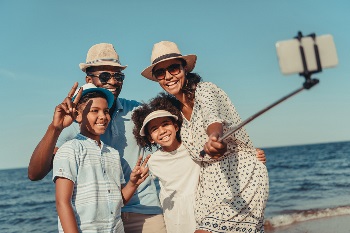 Mother, father, son and daughter standing in front of ocean taking a selfie