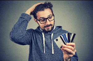 Young man in glasses holding credit cards and looking stressed with increasing debt