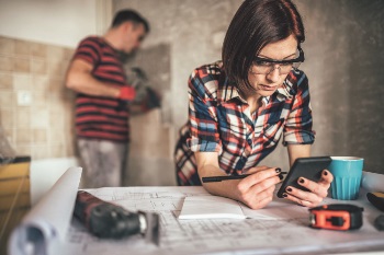 Man hammering into wall and women looking at plans in their home