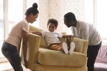 Mom and dad picking up a chair with their toddler sitting on it