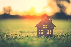 Small wooden home token sitting in grass with sunset behind